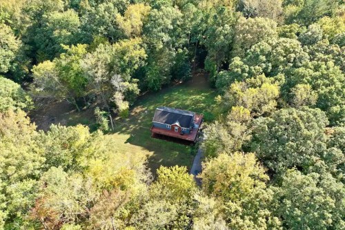Aerial view of a red house surrounded by lush green trees and a grassy area.