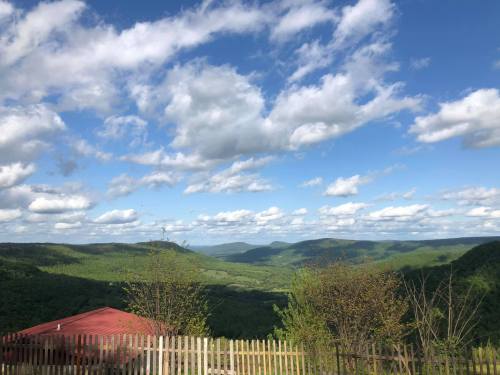 A scenic view of green mountains under a blue sky with fluffy clouds, featuring a red-roofed building in the foreground.