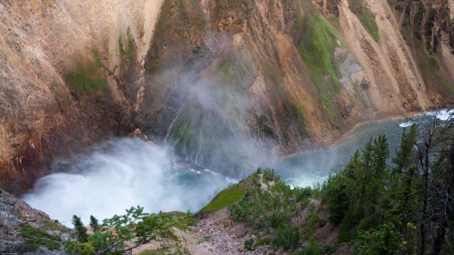A stunning waterfall cascades into a misty pool, surrounded by rocky cliffs and lush greenery.