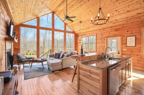 Cozy wooden cabin interior with large windows, a living area, and a kitchen featuring a granite countertop.