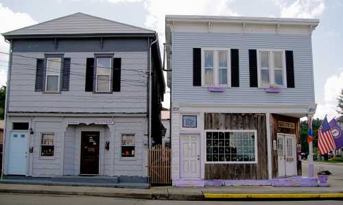 Two adjacent buildings: one gray with black shutters, the other light blue with wooden accents and a small American flag.