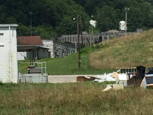 A view of a grassy area with a building in the foreground and a stone wall or fortress in the background.