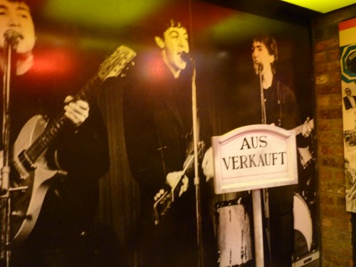 Black and white mural of three musicians performing, with a sign reading "AUS VERKAUFT" in the foreground.