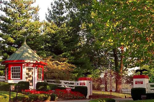 A charming red and white gatehouse surrounded by lush greenery and colorful flowers, leading to a fenced property.