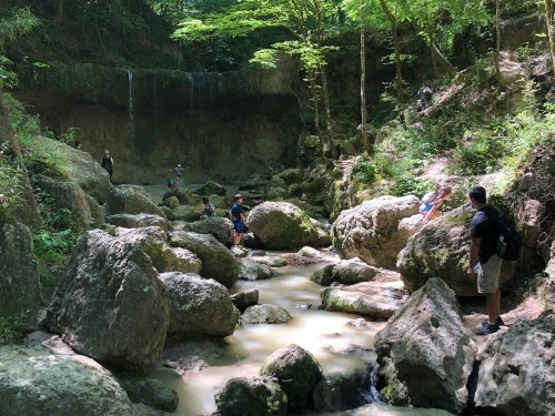 A group of people exploring a rocky stream surrounded by lush greenery and a waterfall in the background.
