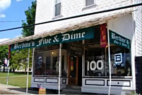 A storefront of Berdine's Five & Dime, featuring a green awning and large windows displaying various items.