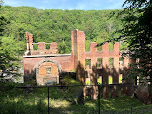Ruins of a brick building surrounded by greenery and trees under a clear blue sky.