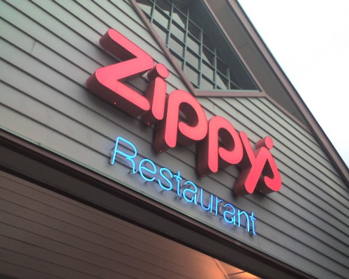 Sign for Zippy's Restaurant, featuring bold red letters and blue neon accents on a building exterior.