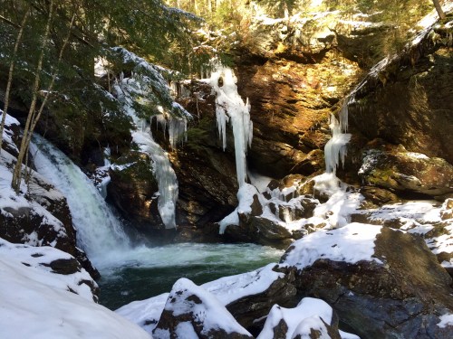 A serene winter scene featuring a waterfall surrounded by snow-covered rocks and icicles hanging from the cliffs.