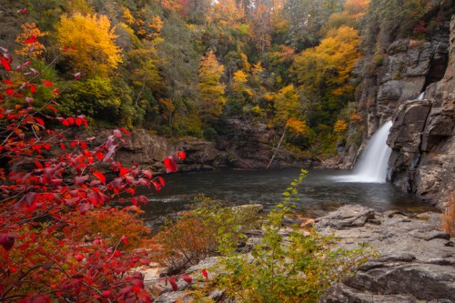 A serene waterfall surrounded by vibrant autumn foliage and rocky terrain, reflecting the beauty of fall.