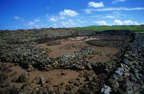 Ancient stone structures on a grassy landscape under a blue sky with scattered clouds.