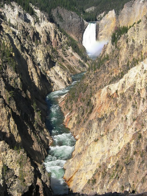 A stunning view of a waterfall cascading into a river, surrounded by steep, rocky cliffs and lush greenery.