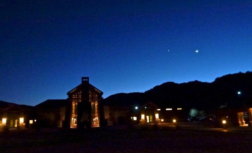 A serene night scene with a silhouette of buildings and mountains under a twilight sky, featuring stars and a crescent moon.