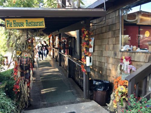 Entrance to Pie House Restaurant, decorated with autumn leaves and scarecrows, with people walking by.