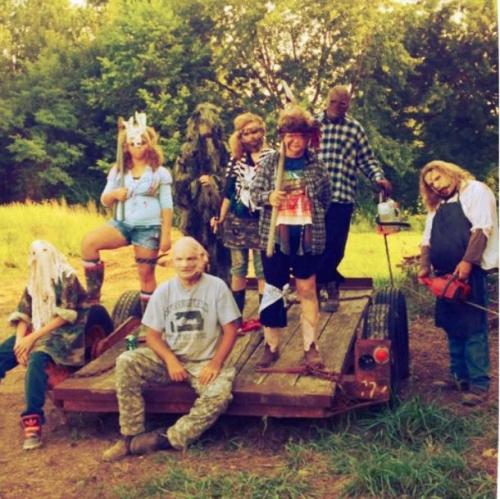 A group of people in costumes and masks posing on a wooden trailer in a wooded area, creating a spooky atmosphere.