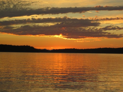 A serene sunset over a calm lake, with vibrant orange and purple hues reflecting on the water's surface.