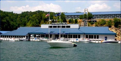 A marina with a blue-roofed building labeled "Jamestown," surrounded by boats on calm water and green hills in the background.