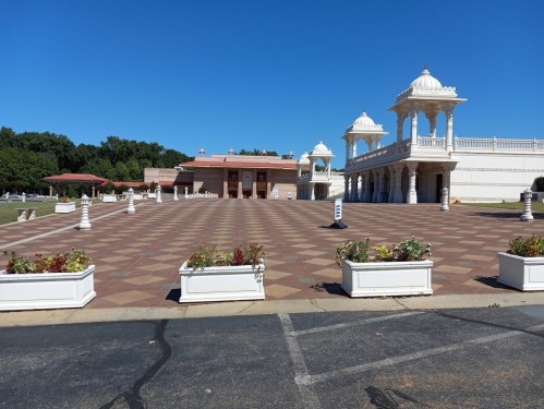 A spacious outdoor area featuring a temple with ornate architecture and flower planters under a clear blue sky.