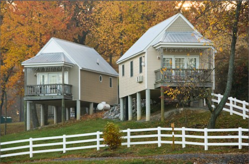 Two charming houses on stilts surrounded by autumn foliage and a white picket fence.