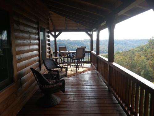 A wooden porch with chairs and a table overlooks a scenic view of rolling hills and trees.