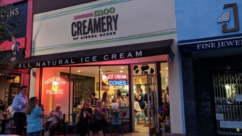 A colorful ice cream shop with people enjoying treats outside and a sign reading "All Natural Ice Cream."