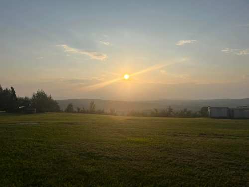 A serene sunset over rolling hills, with a grassy foreground and a clear sky.