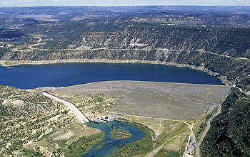 Aerial view of a large reservoir surrounded by rugged terrain and hills, with a dam at the water's edge.