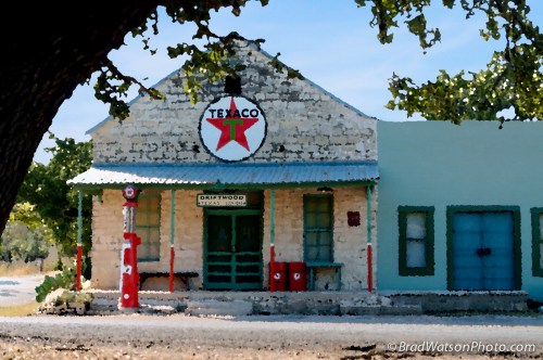 Historic Texaco gas station with vintage pumps, surrounded by trees and a clear blue sky.