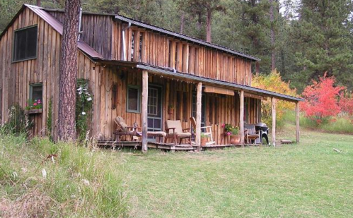 A rustic wooden cabin surrounded by trees and colorful autumn foliage, featuring a porch with chairs.