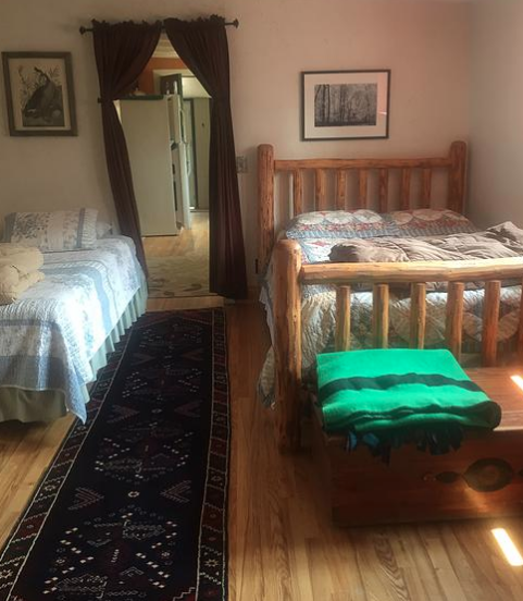 Cozy bedroom with two wooden beds, a patterned rug, and a doorway leading to a kitchen area.