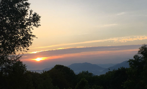 A serene sunset over mountains, with vibrant colors and silhouettes of trees in the foreground.