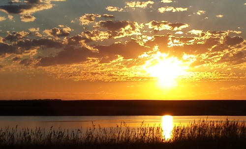 A vibrant sunset over a calm lake, with golden rays illuminating the clouds and reflecting on the water's surface.