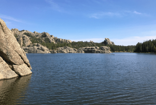 A serene lake surrounded by rocky formations and lush green trees under a clear blue sky.