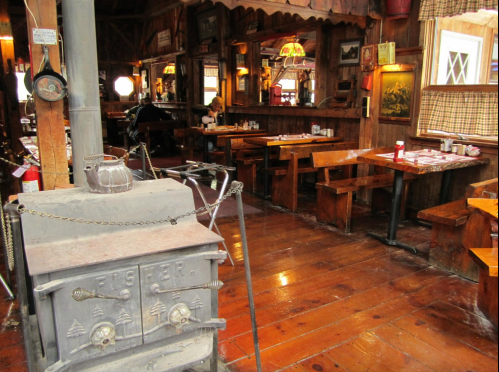 Cozy wooden interior of a rustic restaurant with a vintage stove and wooden tables, creating a warm atmosphere.