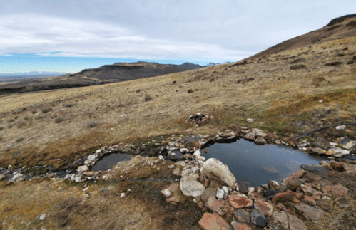 Natural hot springs surrounded by rocky terrain and sparse grassland under a cloudy sky.