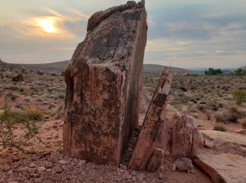 A large, weathered rock formation stands in a desert landscape under a cloudy sunset.