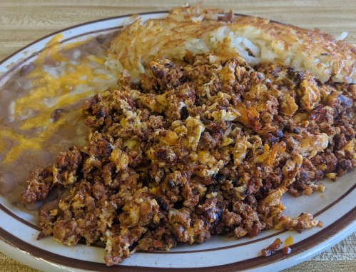 A plate of scrambled chorizo, crispy hash browns, and refried beans topped with cheese.