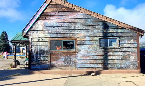 A rustic wooden building with colorful murals on the exterior, set against a clear blue sky.