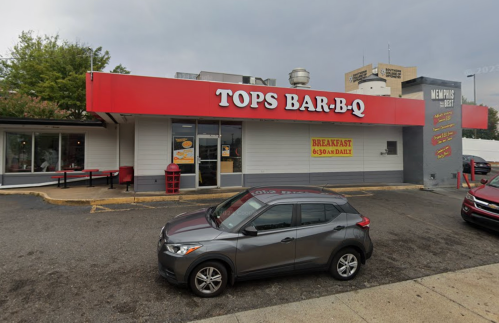Exterior of Tops Bar-B-Q restaurant with a gray car parked in front, cloudy sky overhead.