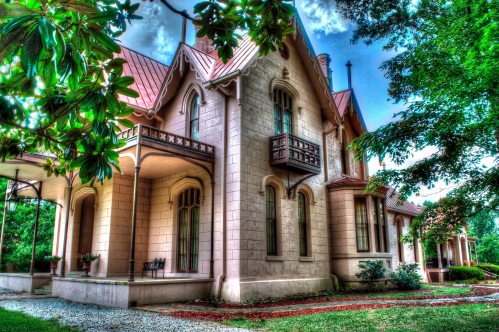 A historic mansion with a pink facade, intricate architecture, and lush greenery surrounding it.
