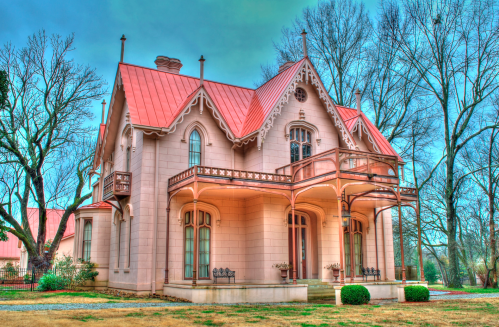 A pink Victorian-style house with a metal roof, featuring balconies and surrounded by bare trees.