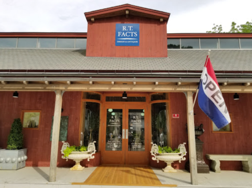 Red wooden building with a sign reading "R.T. FACTS," featuring double doors and an "OPEN" flag.