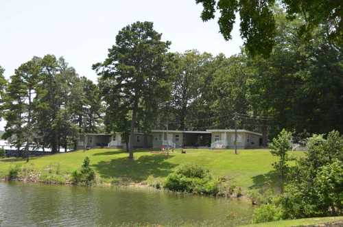 A serene lakeside view featuring a house surrounded by trees and a grassy area, reflecting in the water.