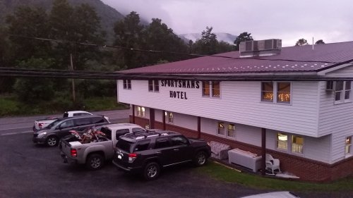 Exterior view of Sportsman's Hotel with parked vehicles and mountains in the background under a cloudy sky.