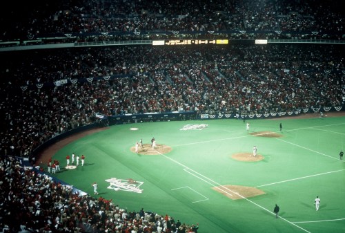 A packed stadium during a baseball game, with players on the field and fans cheering in the stands.