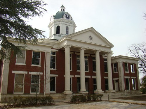 Historic brick building with a clock tower, featuring columns and large windows, set against a cloudy sky.