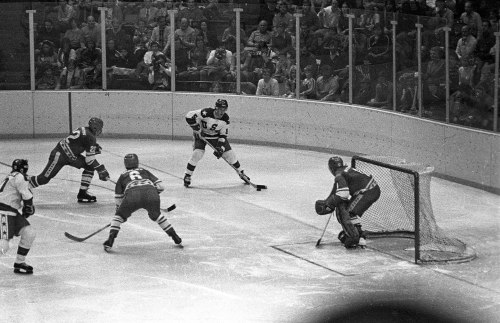 A black and white photo of a hockey game, featuring players on the ice and a goalie in front of the net.