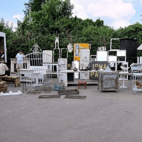 A collection of vintage items and furniture displayed outdoors, with trees and a cloudy sky in the background.