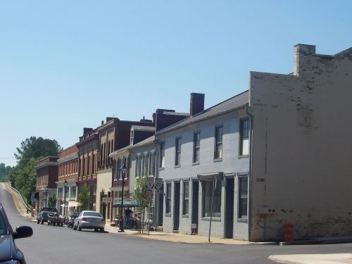 A quiet street lined with historic buildings and parked cars under a clear blue sky.