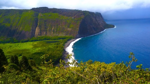 A scenic view of a lush green cliffside meeting a blue ocean under a cloudy sky.